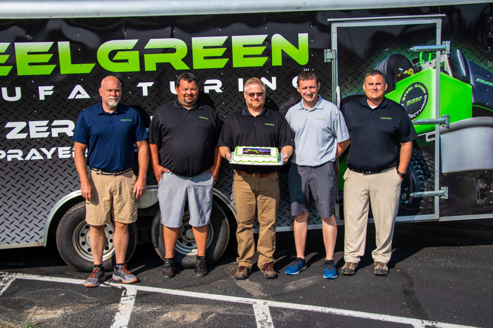 steel green manufacturing team standing in front of trailer with cake